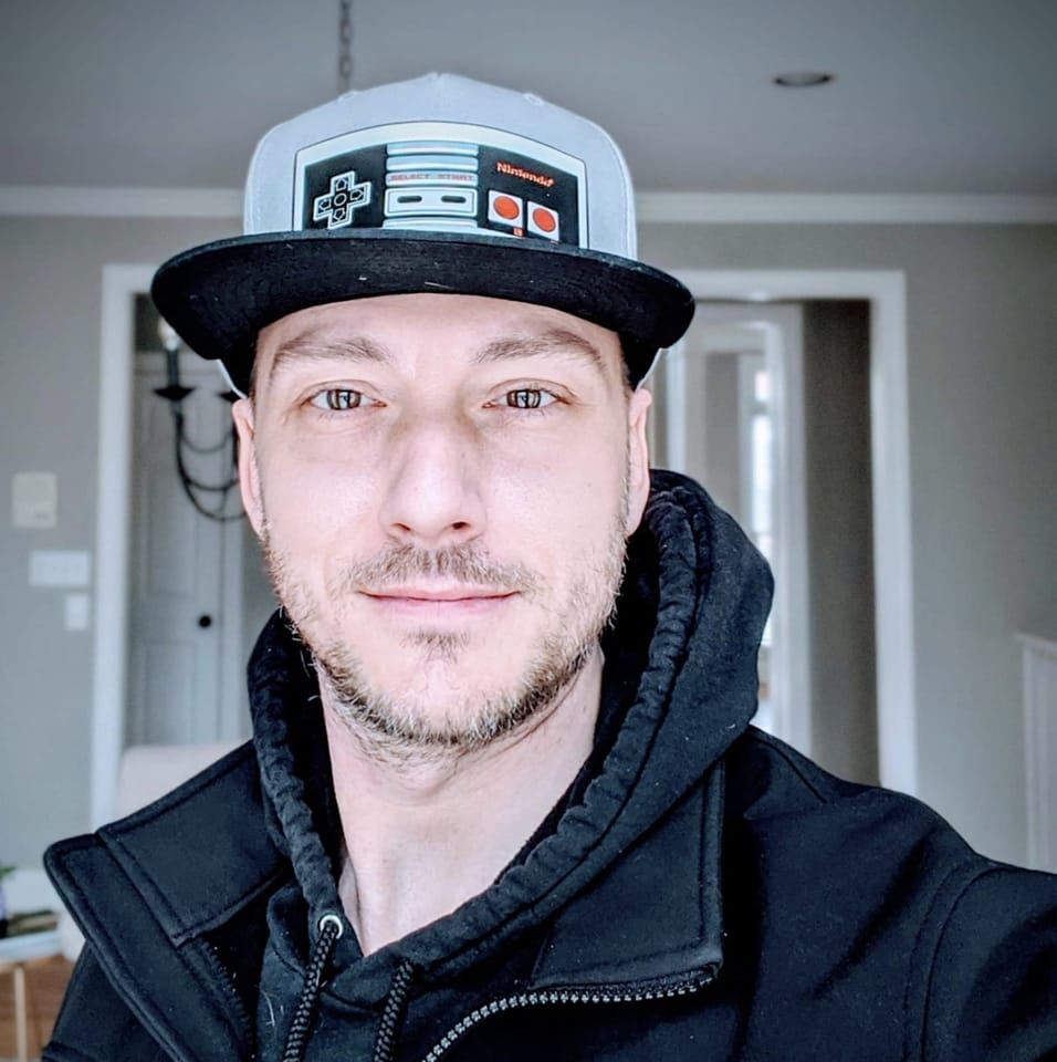 A person wearing a cap with a classic video game controller design is smiling at the camera in this engaging video testimonial.